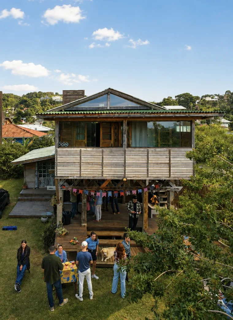 A Casa du Dom vista do quintal: casa de madeira sobre palafitas, com a pista coberta embaixo do deck e o gramado à frente